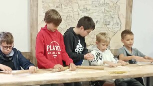 Na drewnianym stole chłopcy wałkują ciasto