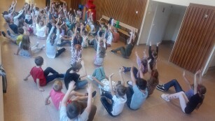 Dzieci siedząc na podłodze podnoszą ręce do góry i wykonują ćwiczenia rozciągające.