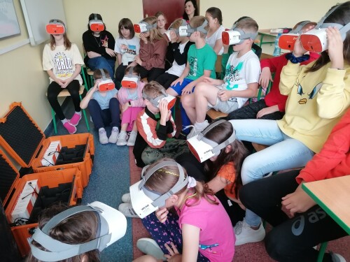 Uczniowie na lekcji siedzą w grupie i korzystają z Gogli VR