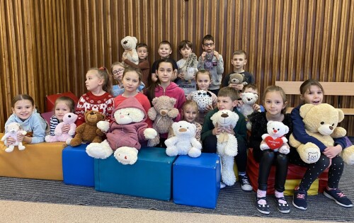 Grupa dzieci pokazuje swoje pluszaki przyniesione do szkoły z okazji Światowego Dnia Pluszowego Misia