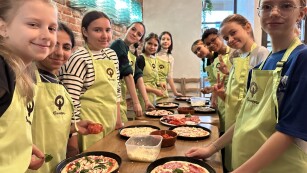 Dziewczęta z klasy 6a stoją przy stole z przygotowanymi przez siebie plackami pizzy