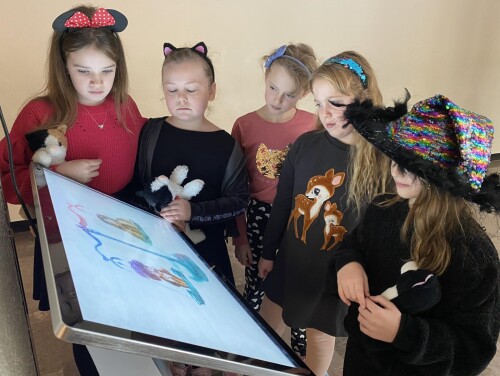 Pięć dziewczynek ogląda animację lubelskich legend na ekranie multimedialnym.