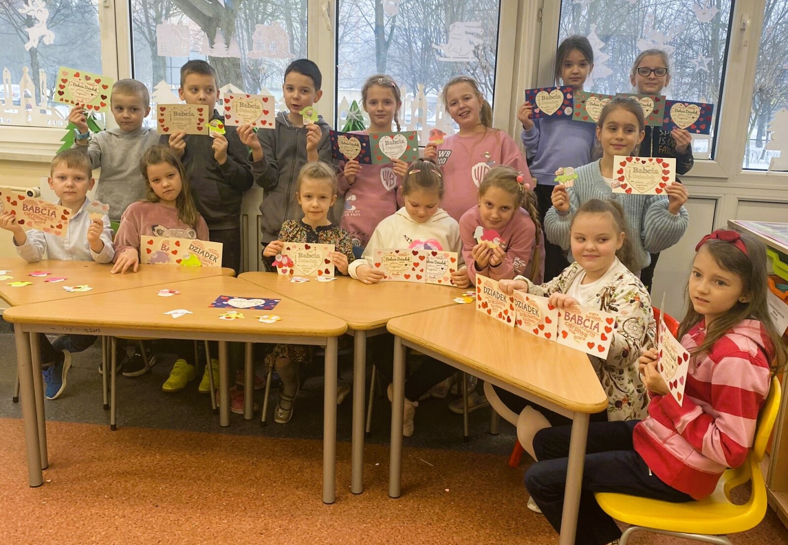 Grupa dzieci prezentuje wykonane przez siebie laurki z sercem oraz babeczki z papieru wykonane z okazji Dnia Babci i Dziadka.