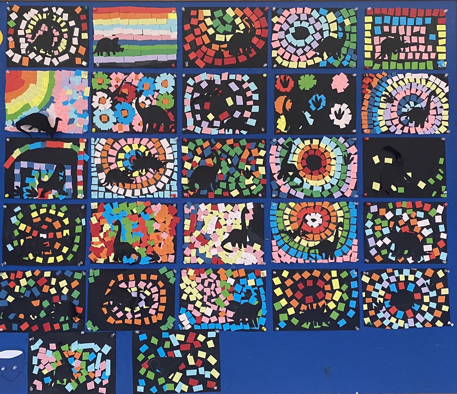 1. Tablica z pracami dzieci – technika kolorowa mozaika i czarne dinozaury.