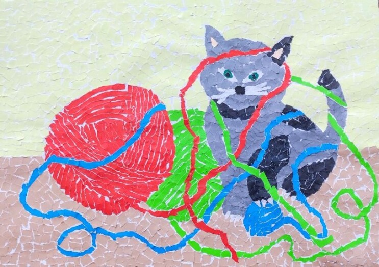 Praca plastyczna przedstawiająca kota zaplątanego w kolorowe nici wyciągnięte z kulek wełny.