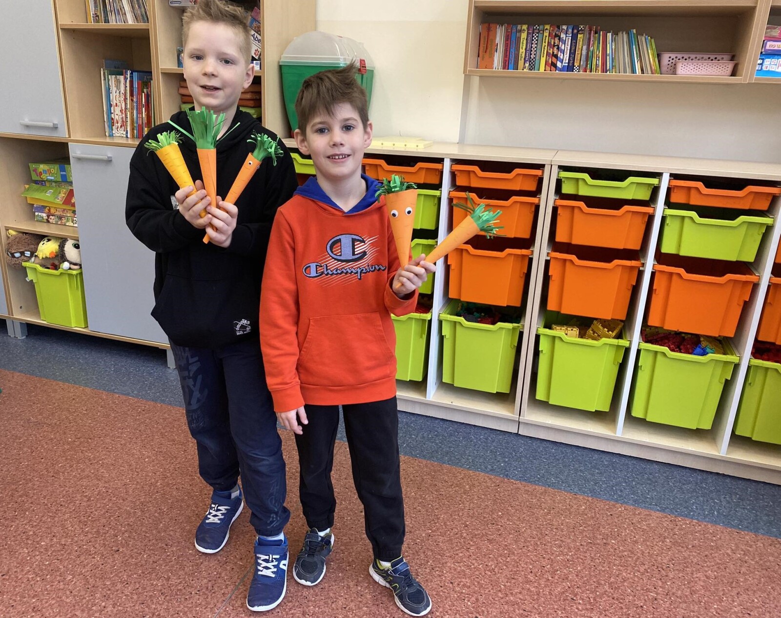 Dwaj chłopcy trzymają w dłoniach papierowe  marchewki wykonane w świetlicy podczas zajęć plastycznych z okazji Dnia Marchewki.